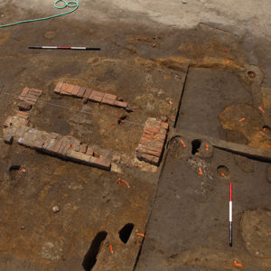 Aerial view of an excavated area showing several features and a square brick foundation