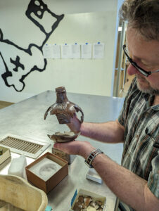 Archaeological Conservator Dr. Chris Wilkins holds the top and bottom portions of the Bartmann jug he's piecing together.