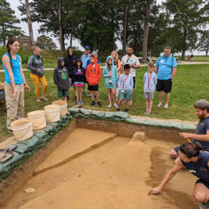 Field School student Lianna Styles explains the north field excavations to guests.