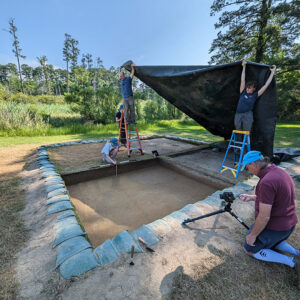 Senior Staff Archaeologist Sean Romo and Archaeological Field Technician Brenna Fennessey shade the clay borrow pit while Senior Staff Archaeologist Dr. Chuck Durfor takes record shots.