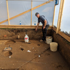 Senior Staff Archaeologist Sean Romo points to one of the mud and stud structure postholes inside the burial structure.