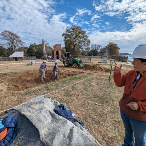 Senior Staff Archaeologist Mary Anna Hartley describes the backfilling process at the burial site as the archaeological team fills it in at left.