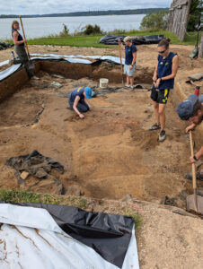 The archaeological team has removed much of the backfilled soil from the excavations in the early 2000s. The burials are the darker rectangles oriented horizontally in this photo.