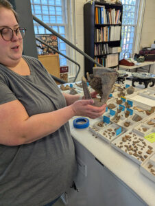 Collections Assistant Lauren Stephens holds a large crucible from the collection. Many other crucibles and crucible sherds can be seen just to her left.