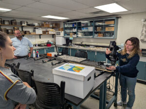 University of Connecticut undergrad Cassie Aimetti demonstrates the use of a macropod scanner that is used to photograph vibracore samples.