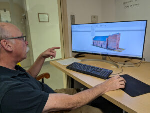 Senior Staff Archaeologist Dr. Chuck Durfor demonstrates the Memorial Church and Church Tower model that he and Site Supervisor Anna Shackelford are working to complete.