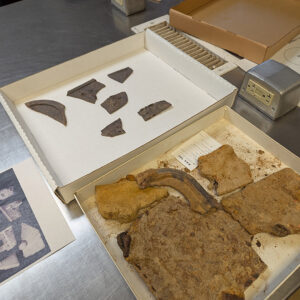 Pieces of the 19th-century oven. Assistant Conservator Jo Hoppe has removed corrosion from the pieces in the top box. In the bottom box are fragments in varying states of conservation.