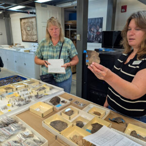 Senior Curator Leah Stricker holds a partially mended Native ceramic vessel. She's sharing artifacts during an update for volunteers.