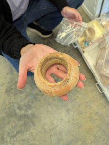 A Spanish olive jar rim piece is held by Associate Curator Janene Johnston. This piece was found during the Seawall excavations of 2021.
