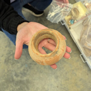 A Spanish olive jar rim piece is held by Associate Curator Janene Johnston. This piece was found during the Seawall excavations of 2021.