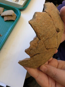 Assistant Conservator Jo Hoppe holds the globular-shaped Virginia Indian jar that she's remending after discovering part of its adhesive was losing its grip. The jar will go back on display in the Archaearium after Jo is finished.