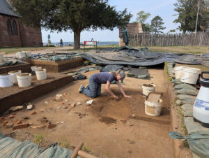 Archaeological Field Technician Katie Griffith excavates the top layers of the well. A plethora of architectural artifacts can be seen to her right, likely purposely discarded there.