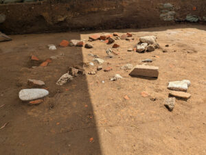 The architectural materials found in the clay cap of the well. The outline of the clay cap was scored by an archaeologist to make it easier to see the difference between the lighter, mottled clay of the cap and the darker, more uniform soil of the original well fill surrounding it.