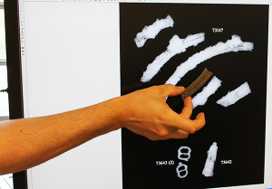 Hand holding an iron fragment up to an x-ray of an assortment of iron artifacts