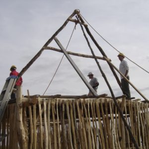 Three men standing atop a half-built wooden structure with a raised roof frame