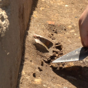 trowel being used to excavate the base of an earthenware cup