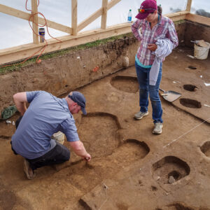 Senior Staff Archaeologists Sean Romo and Mary Anna Hartley examine a posthole that cuts one of the burials.