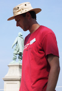 Archaeologist standing in front of a statue and looking down at an item off-camera