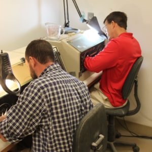 Two conservators seated at air abrasion machines