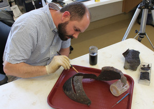 conservator applying solution to a corroded close helmet on a tray
