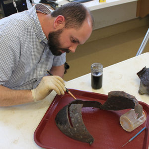conservator applying solution to a corroded close helmet on a tray
