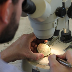 Conservator looking through a microscope to remove corrosion on an artifact