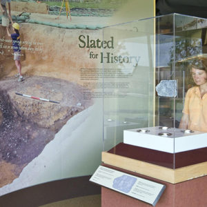 Woman examines an inscribed piece of slate in a museum case in front of exhibit panels