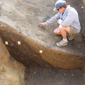 archaeologist using a trowel to clean layers of stratigraphy