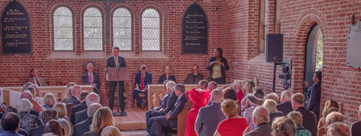 Speaker at podium talks to seated group in brick church