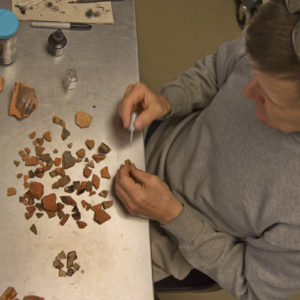 Conservator uses a small brush to paint ceramic sherds with B72