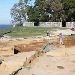 Archaeologists standing in and walking around a large excavation area