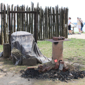 Small recreated iron bloomery in front of a palisade