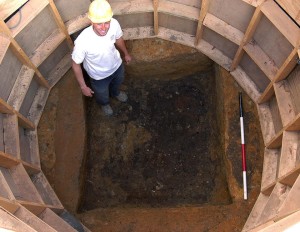 Archaeologist standing in excavated square-shaped well surrounded by circular supporting wooden frame