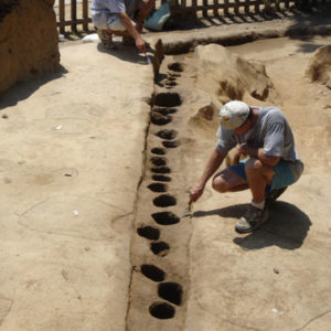 Two archaeologists troweling along a line of excavated postholes