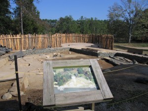 Sign with image of digitally-reconstructed James fort buildings in front of excavation unit and palisade