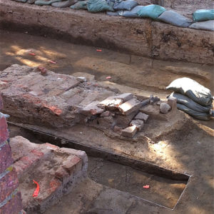 three excavation trenches and sections of bricks with archaeologist screening artifacts in the background