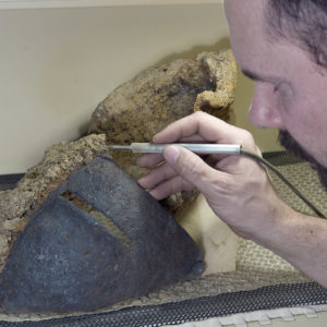Director of Collections and Conservation Michael Lavin uses air abrasion to remove rust from the close helm