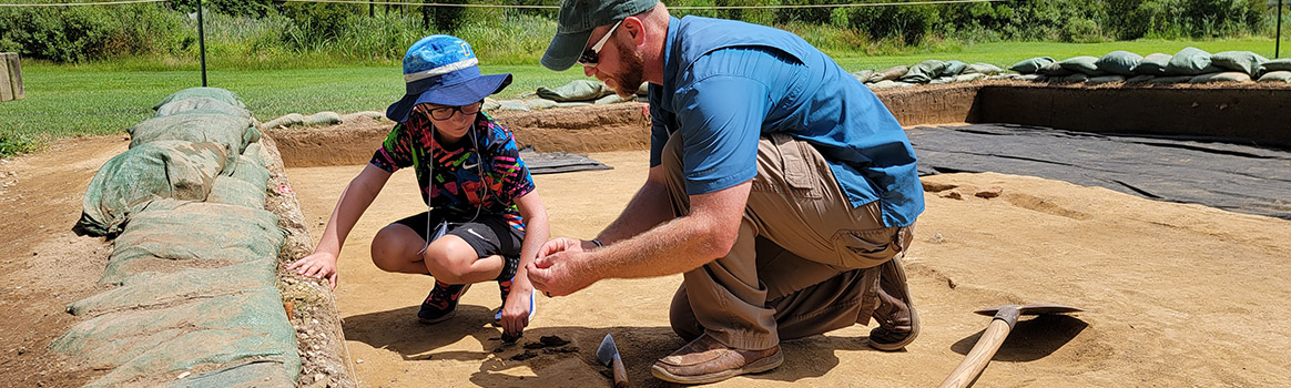 Senior Staff Archaeologist Sean Romo instructs a camper on the troweling process.