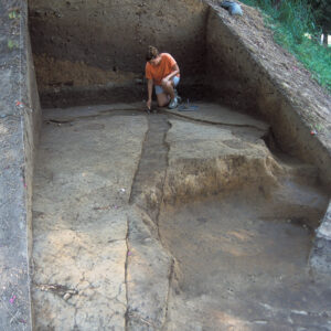 In this 2009 photo archaeologist Jamie May points to the spot where the 1608 palisade extension (coming towards the photographer) meets the eastern palisade wall (towards the photographer's left) and the curve of the north bulwark (to the photographer's right). The earthworks behind Jamie are part of Confederate Fort Pocahontas, built on the same high ground that the colonists used to build their fort.