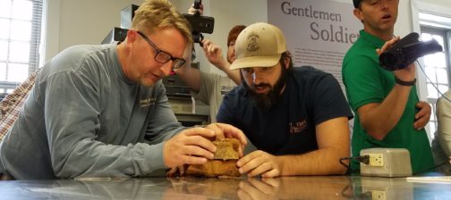 Staff examine artifact on lab table while others film
