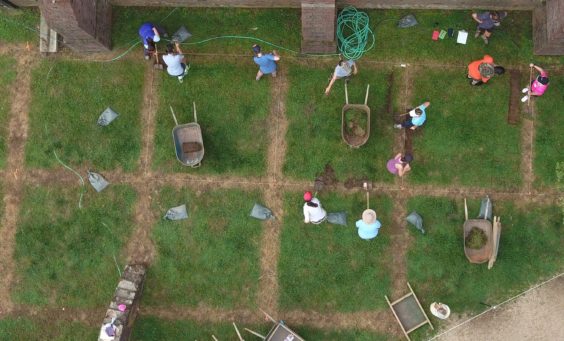 Aerial view of wheelbarrows and students shoveling in square excavation units