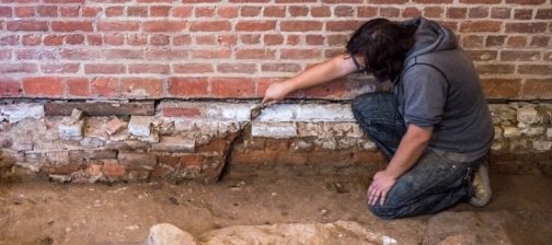Archaeologist gestures with trowel to brick foundations