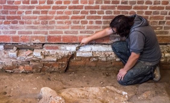 Archaeologist gestures with trowel to brick foundations