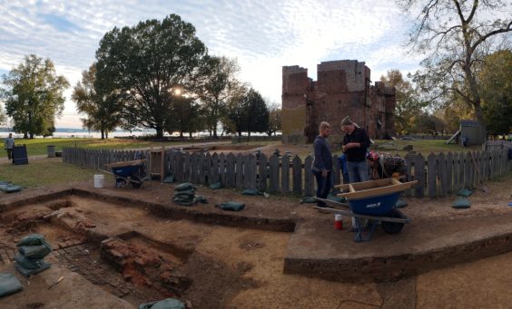Archaeologists examine artifact while standing in excavations in front of brick ruins