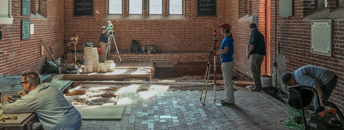 Archaeologists recording the location of excavated features within the floor of a brick church