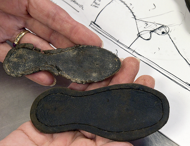 Hands holding leather soles to a child's shoe in front of a sketch drawing of a recreation