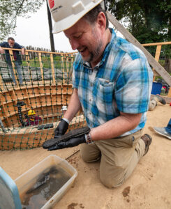 Archaeological Conservator Dr. Chris Wilkins examines the just-excavated leather shoe sole.