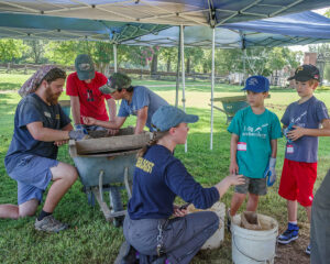 Archaeological Field Technician Josh Barber and Staff Archaeologist Natalie Reid assist some of the campers with screening.